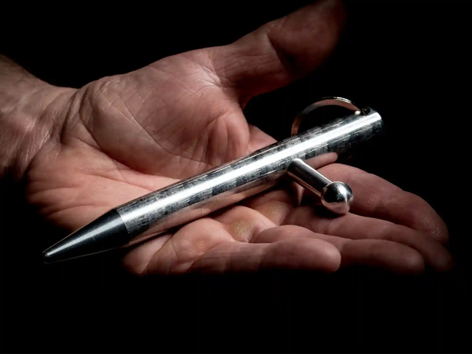 a silver Kubotee self defence tool in the open Hand of a man
